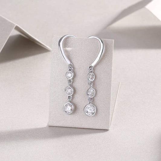 Silver earrings with clear stones on a gray card against a light gray background